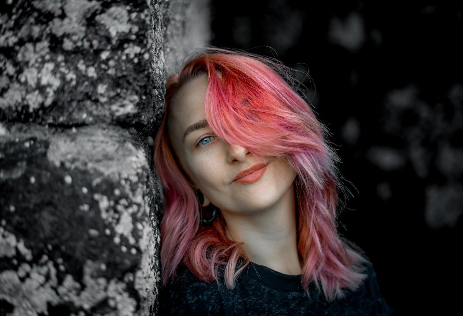 A woman with pink hair standing next to a stone wall